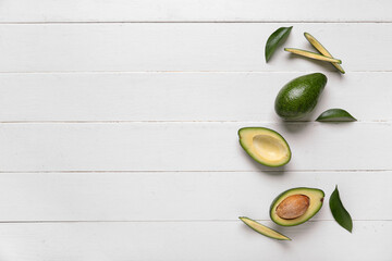 Fresh ripe avocados and leaves on white wooden background