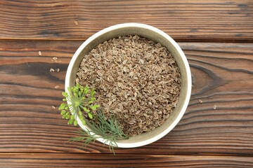 Bowl of dry seeds and fresh dill on wooden table, top view