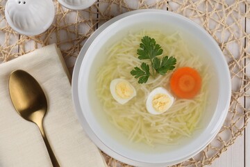 Tasty soup with noodles, egg, carrot and parsley in bowl served on white wooden table, flat lay