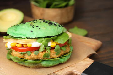 Tasty green vegan burger with vegetables, patty and microgreens on wooden table, closeup. Space for text