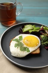 Plate with tasty fried egg, slice of bread and salad on light blue wooden table, closeup