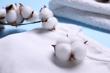 Cotton branch with fluffy flowers and white t-shirt on light blue background, closeup