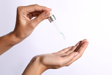 Woman applying cosmetic serum onto her hand on white background, closeup