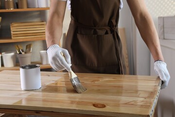 Man varnishing wooden surface with brush indoors, closeup