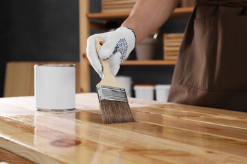 Man varnishing wooden surface with brush indoors, closeup