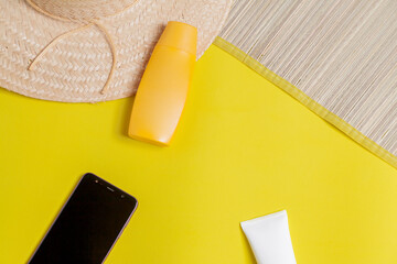 Beach accessories. Mat and hat with sunscreen bottles and smartphone on colorful background. Beach accessories concept. Vacation concept. Space for text.