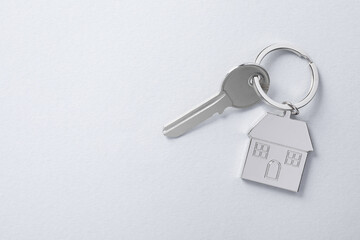Key with keychain in shape of house on light background, top view. Space for text
