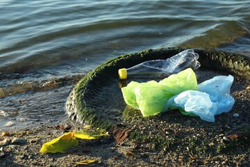 Plastic trash and tire on sand near water. Environment pollution