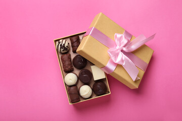 Open box with delicious chocolate candies on pink background, top view