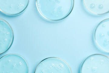 Frame of Petri dishes with liquid samples on light blue background, flat lay. Space for text