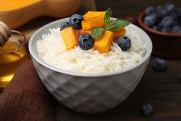 Bowl of delicious rice porridge with blueberries and pumpkin on wooden table, closeup
