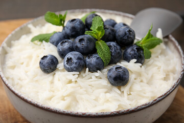 Bowl of delicious rice porridge with blueberries and mint on table, closeup