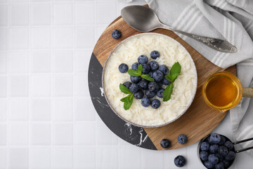 Bowl of delicious rice porridge with blueberries and mint served on white tiled table, flat lay. Space for text