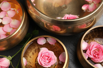 Tibetan singing bowls with water and beautiful rose flowers on table, above view