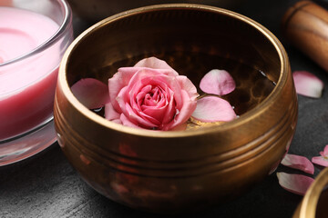 Tibetan singing bowl with water, beautiful rose flowers and scented candle on table, closeup