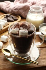 Cup of aromatic hot chocolate with marshmallows and cocoa powder served on wooden table, closeup