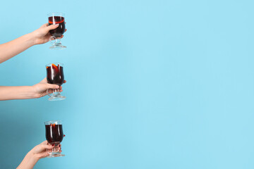 Female hands with glasses of warm mulled wine on blue background