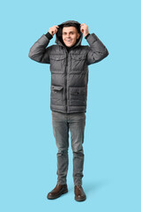 Young man in stylish puffer jacket on blue background