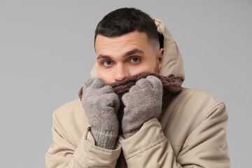 Young man in stylish puffer jacket and scarf on grey background