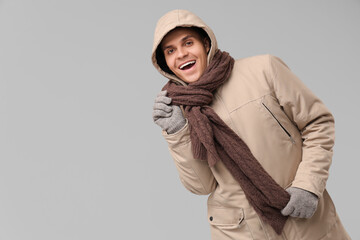 Young man in stylish puffer jacket and scarf on grey background