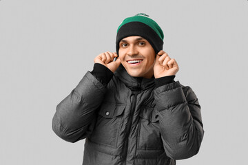 Young man in stylish puffer jacket and hat on grey background