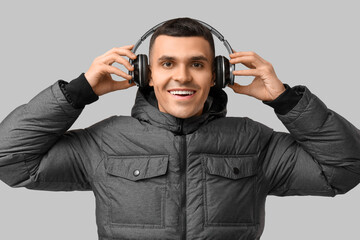 Young man in stylish puffer jacket and headphones on grey background