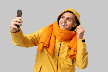 Young man in yellow stylish jacket and scarf taking selfie on grey background