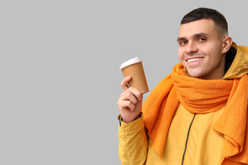 Young man in yellow stylish jacket and scarf with paper cup of coffee on grey background