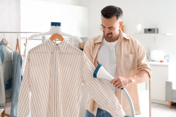 Handsome man steaming shirt with modern steamer at home