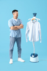 Handsome man with modern steamer and clothes on blue background
