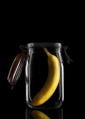 A Banana inside a glass storage or canning jar isolated on black with reflection, with lid open.