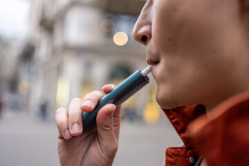 Close up of a man vaping with electronic cigarette outdoor on street.