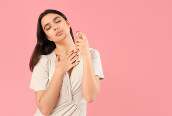 Young woman applying perfume on pink background