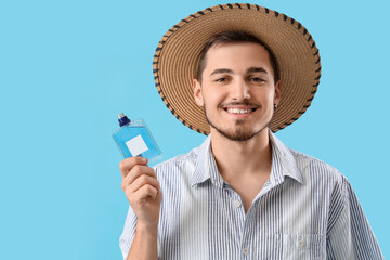 Young man in straw hat with perfume on blue background