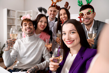 Happy young colleagues with champagne taking selfie at New Year party in office