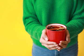 Young woman with cup of hot mulled wine on yellow background