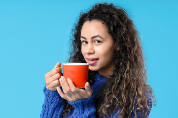 Beautiful young African-American woman with cup of hot mulled wine on blue background