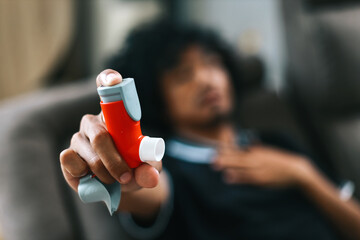 Man holding and showing asthma inhaler while sitting on couch at home Medical equipment concept