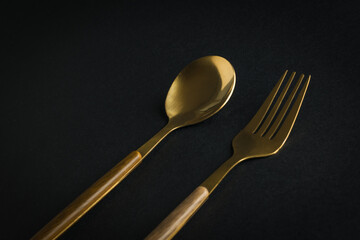 Gold-plated spoon and fork on a black background.