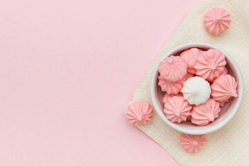 Top view of a bowl with meringue on a fabric on a pink background. Space for text.