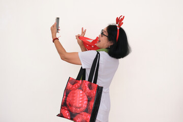 An Asian woman wearing a white t-shirt and christmas-themed accessory is carrying shopping bags...