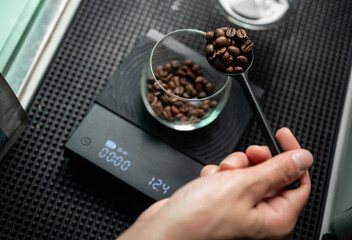 Barista holding a tablespoon roasted coffee beans before adding into a glass cup for measuring weight.