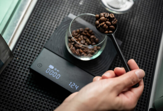 Barista holding a tablespoon roasted coffee beans before adding into a glass cup for measuring weight.