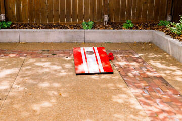 Cornhole, a lawn game with a board with red and white stripes and a red fabric bean bag
