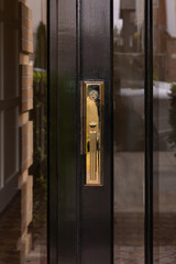 close up of a door handle, gold plated, shiny black door with small frosted glass windows.