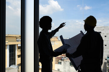 Silhouettes of foreman and builder discussing construction plan