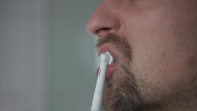Man brushes his teeth with an electrical tootbrush at morning bathroom before work. Male uses an electric sonic dental cleaning brush. Daily dental hygiene and oral health with eletrical teethbrush. 