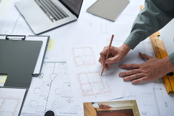 Hands of construction worker checking details of blueprint on his desk