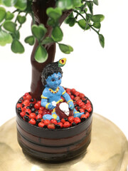 a colorful doll statue of cute baby sri krishna in blue eating butter out of a pot under a tree, an...