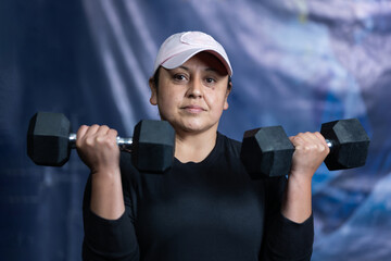 Middle-aged latina woman exercising with two dumbbells